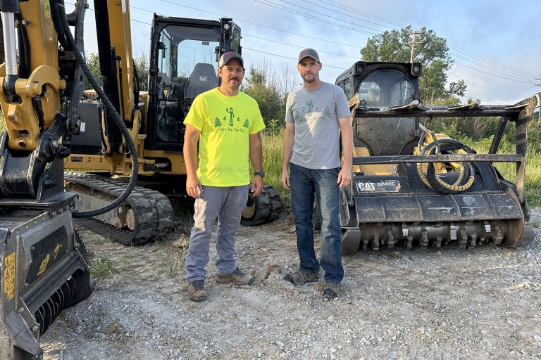 Two team members stand with excavator